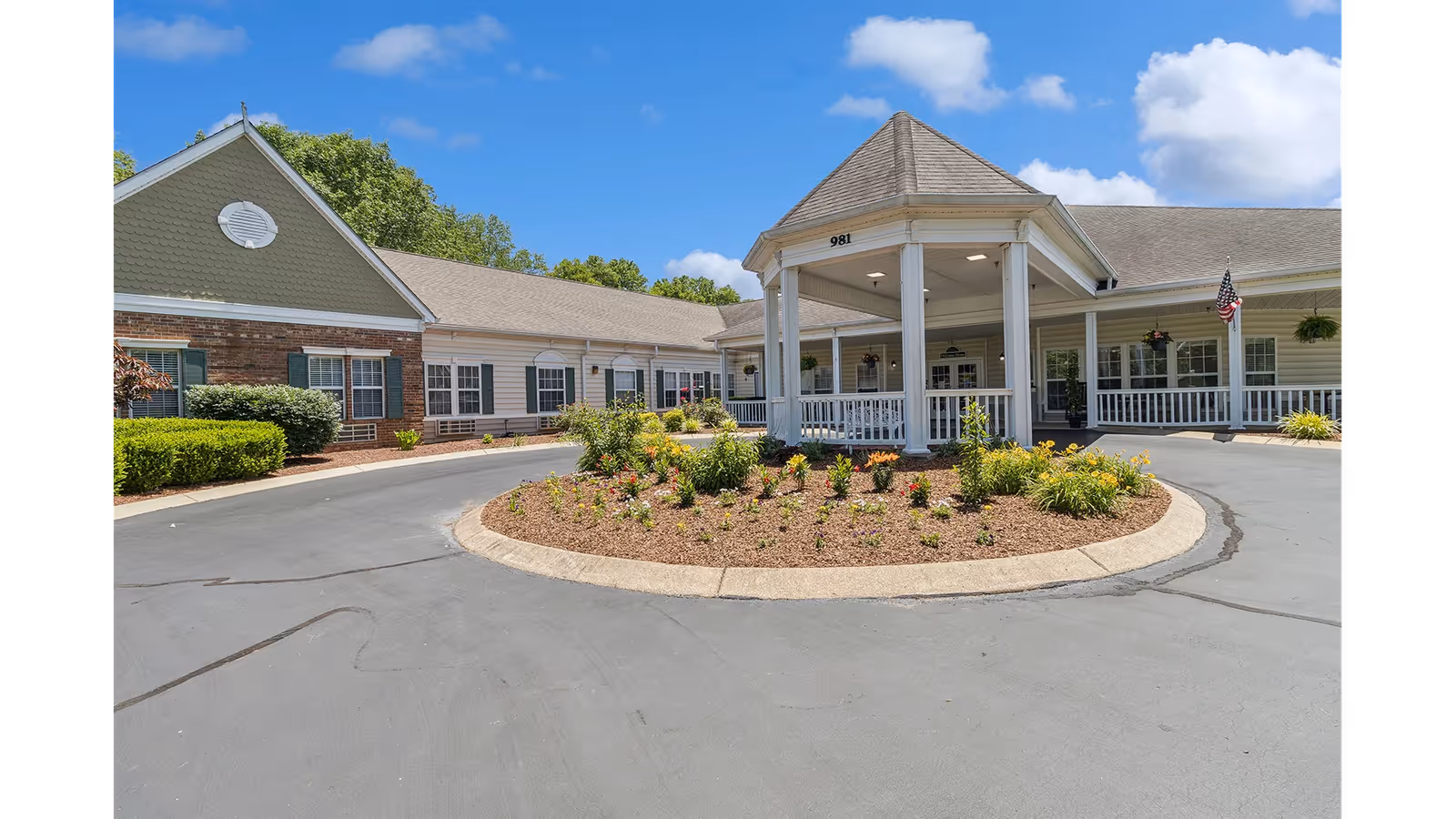 Front entrance of a single-story senior living building with a covered portico, circular driveway, and landscaped center island.