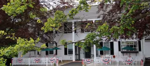White nursing home exterior with green awnings, bunting, and a white picket fence.