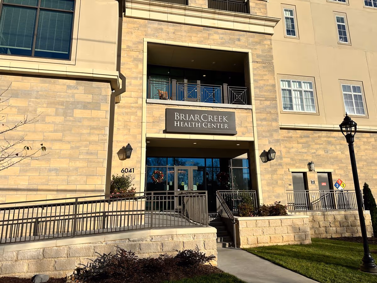 Entrance to the BriarCreek Health Center with a stone facade, sign above glass doors, an access ramp, and the street number 6041 visible.