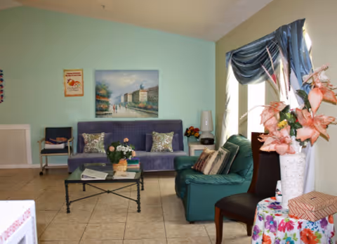A cozy living room in a senior facility with pastel walls, couches, and plants.