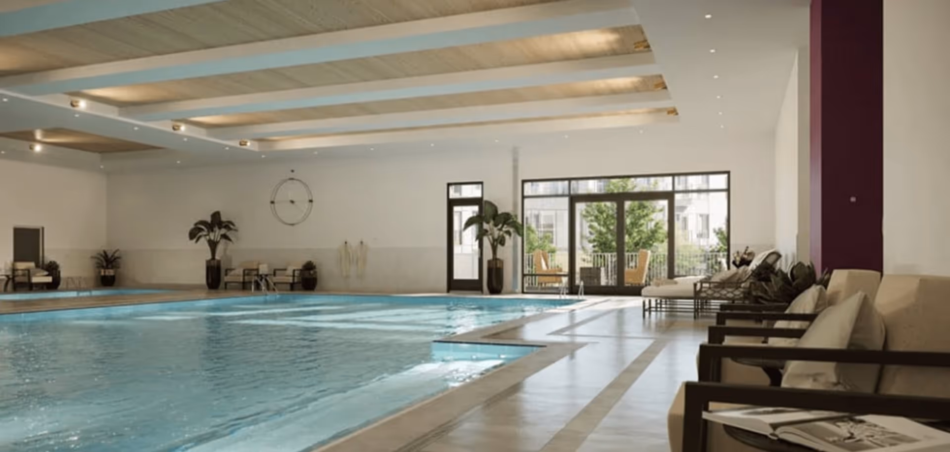 Indoor swimming pool with lounge chairs, potted plants, and large windows opening to an outdoor patio.