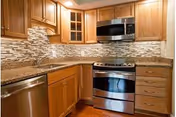 Modern kitchen with wooden cabinets, granite countertops, stainless steel dishwasher, stove, and microwave. The backsplash features a mosaic tile design in neutral tones.