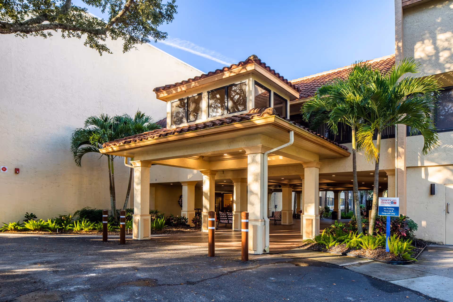 Entrance of American House Sarasota senior living facility with palm trees and green landscaping.