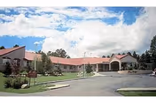 Front exterior of a single-story rehabilitation and healthcare building with a covered entrance, red roof, and landscaped lawn under a partly cloudy sky.