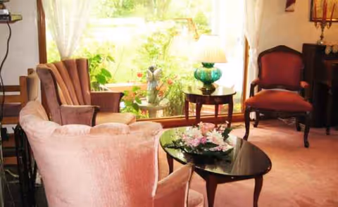 Cozy living room with pink upholstered seating, glass coffee table, flowers, and sunlight.