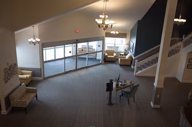 Spacious senior living lobby with seating areas, chandeliers, glass entry doors and a staircase.