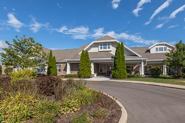 Front exterior view of Brookdale Kenosha facility with a driveway, landscaped garden, and clear blue sky.