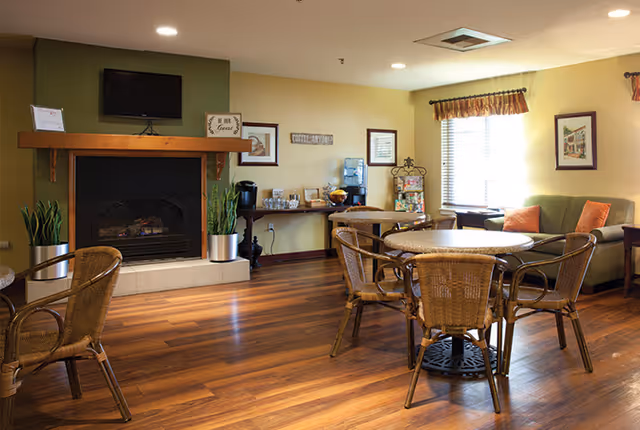 Common lounge with round wicker dining tables and chairs, a fireplace, a sofa, and a refreshment station.