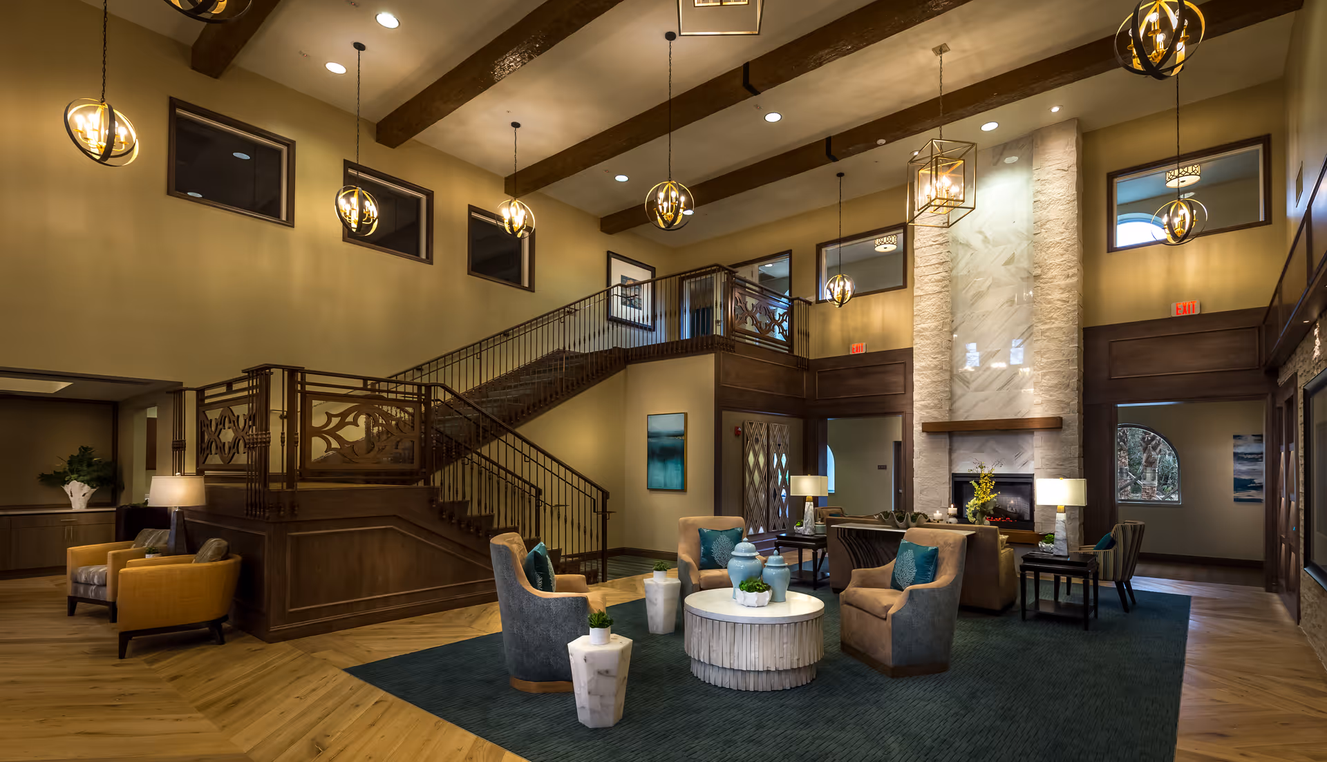 Spacious two-story lobby/lounge with a central seating area, fireplace, and a decorative staircase under pendant lighting.