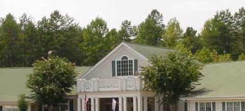 Front view of a single-story senior living building with a green roof and trees.
