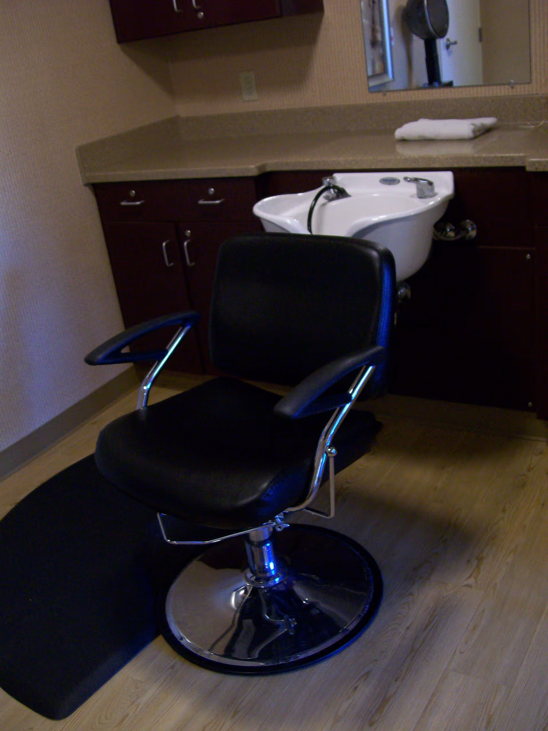 A black salon chair in front of a hair-washing sink and cabinetry inside a room.