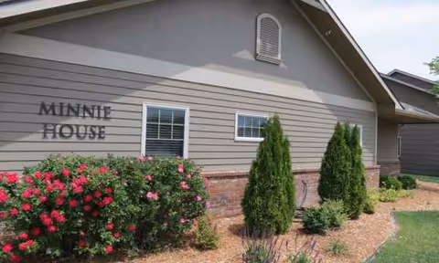 Front exterior of a senior living building with landscaped shrubs and blooming roses.