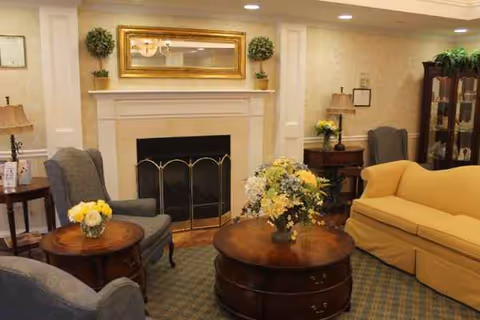 Cozy senior living lounge with fireplace, seating, and floral arrangements.