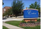Blue Embers Retirement Community sign with sidewalk, trees, and brick building behind