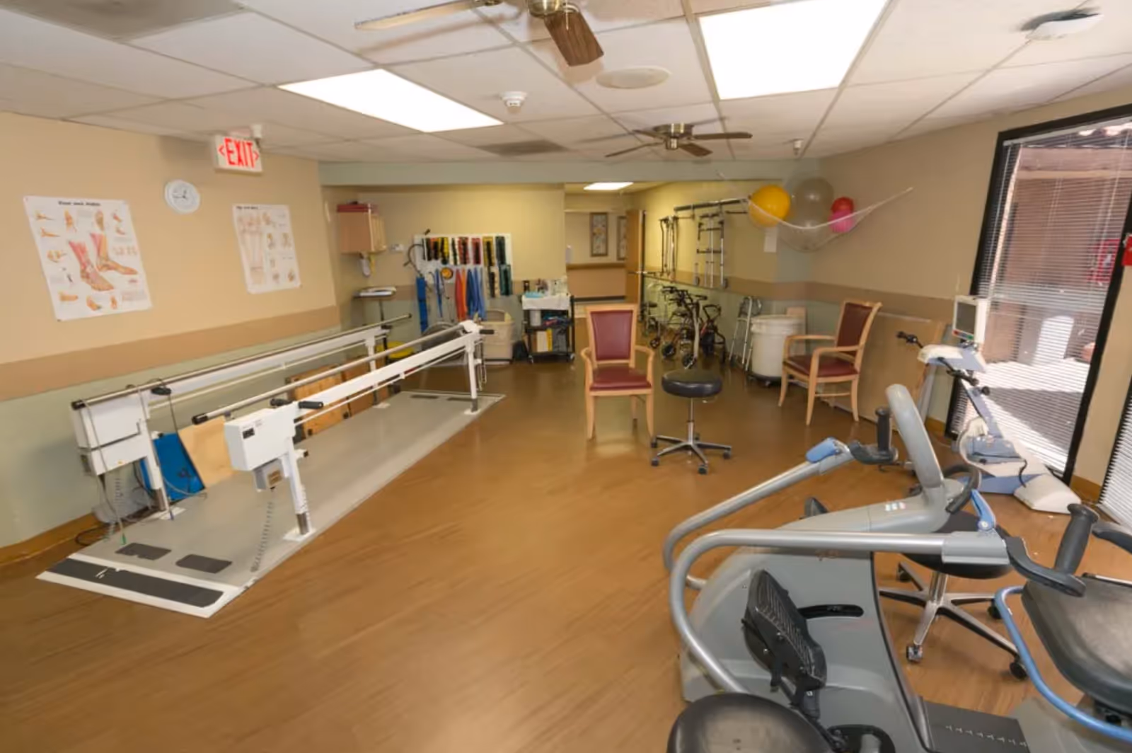 Rehabilitation/exercise room with parallel bars, cardio machines, chairs and mobility aids.