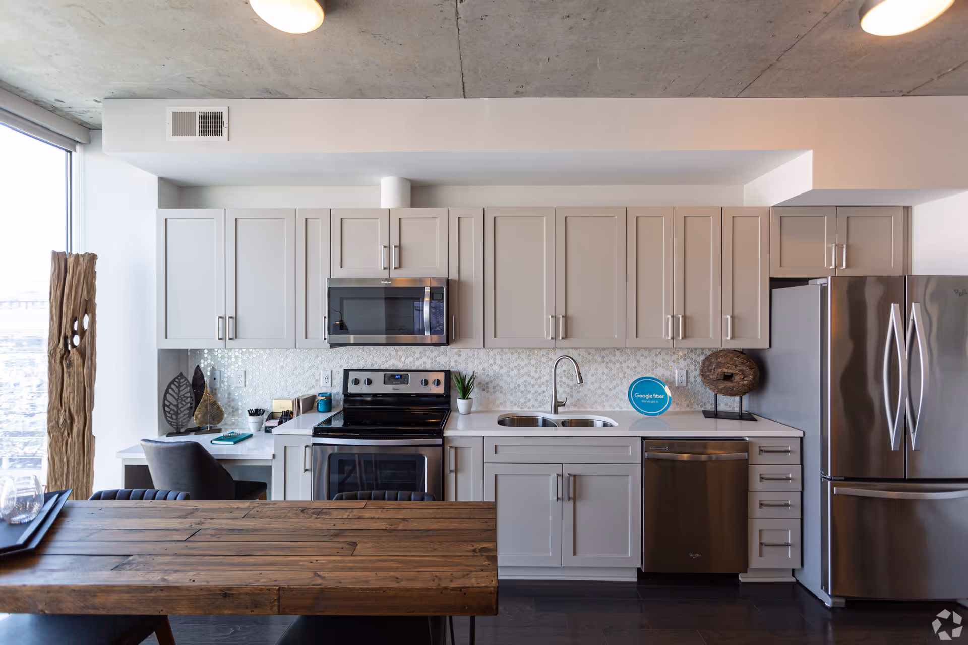 Bright modern kitchen with light gray cabinets, stainless steel appliances, a double sink and a rustic wooden dining table.