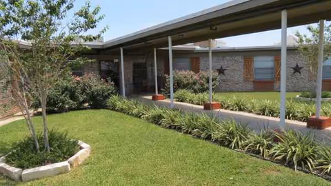 Exterior view of Eagle Pass Nursing and Rehabilitation showing a covered walkway and landscaped courtyard.