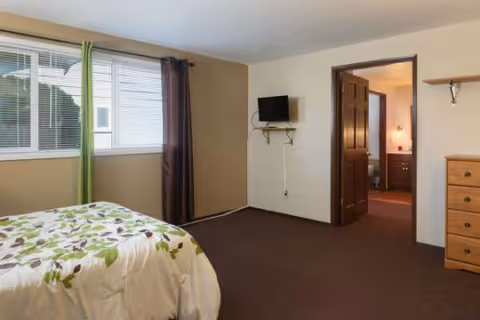 A bedroom in a senior living facility with a bed, window, and dresser.