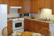 Cozy kitchen with wooden cabinets, white appliances, a double sink, and a small round dining table with chairs.