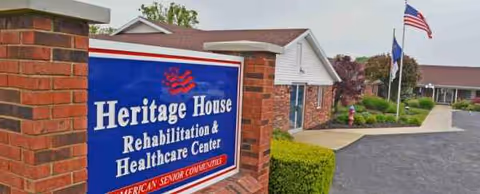 Heritage House Rehabilitation and Healthcare Center sign beside brick entrance with flags