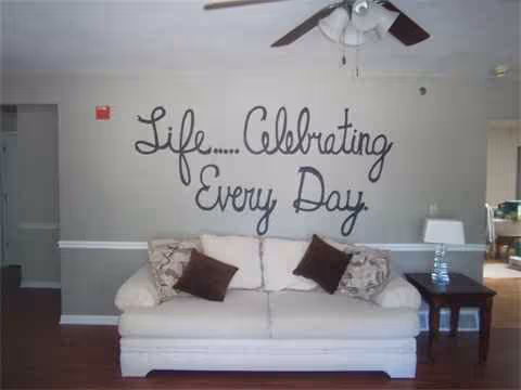 White sofa with brown cushions in a lounge; wall reads 'Life... Celebrating Every Day'.