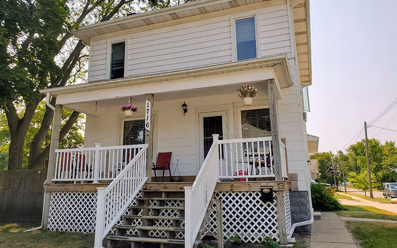 Two-story white house with a front porch, stairs, and hanging flower pots.