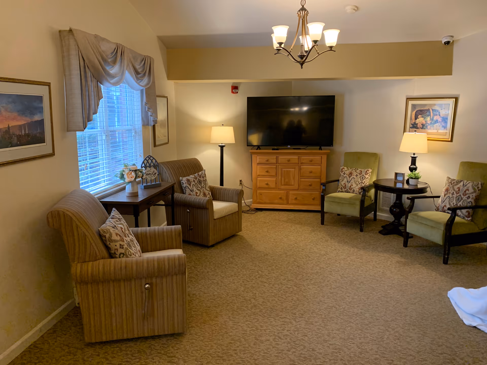 Common lounge area featuring a television on a wooden cabinet, armchairs, side tables, and lamps.