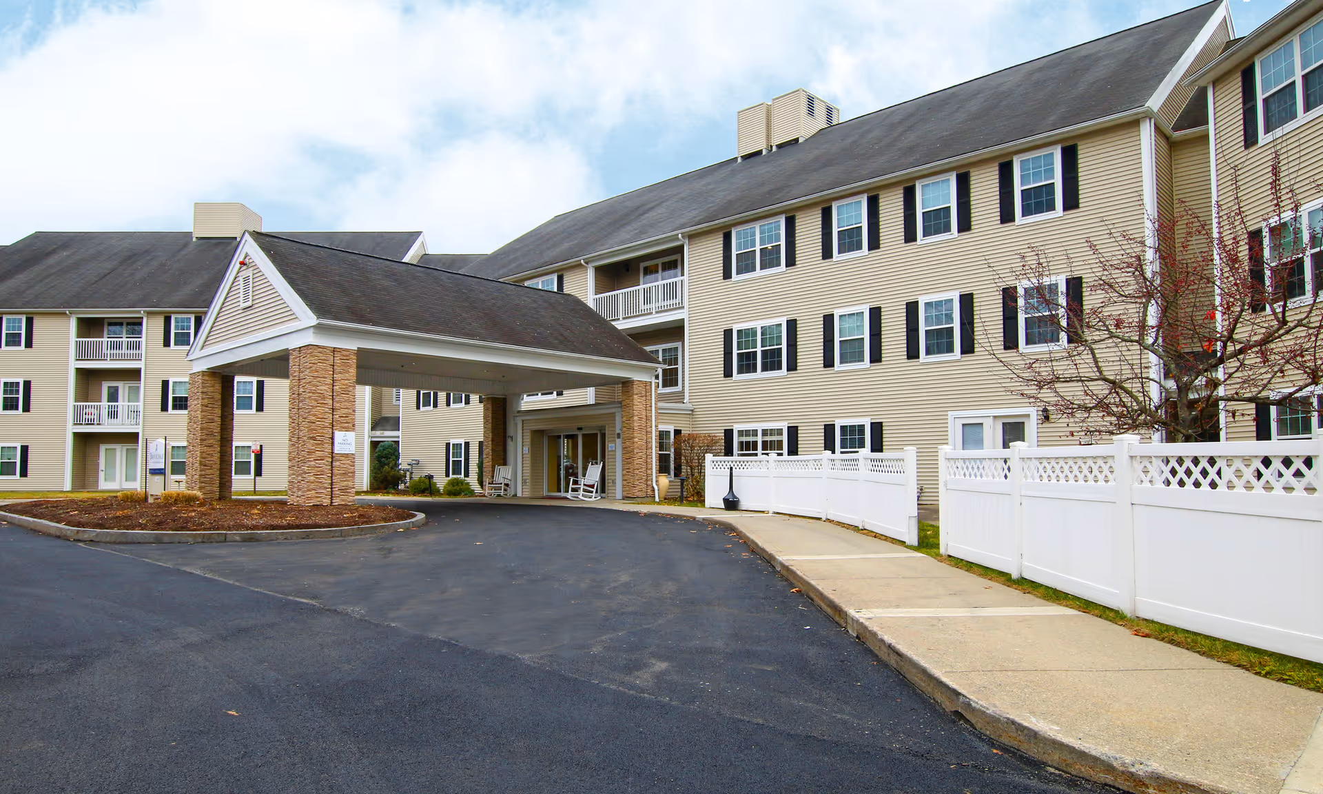 Exterior view of a Brookdale Eddy Pond senior living building with covered entrance and white fence.