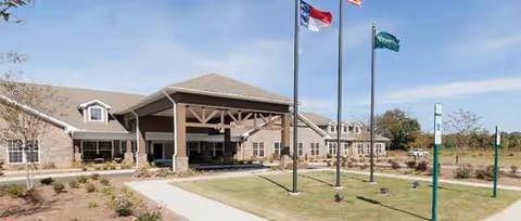 Senior living facility exterior featuring a covered entrance, flagpoles, and manicured landscaping.