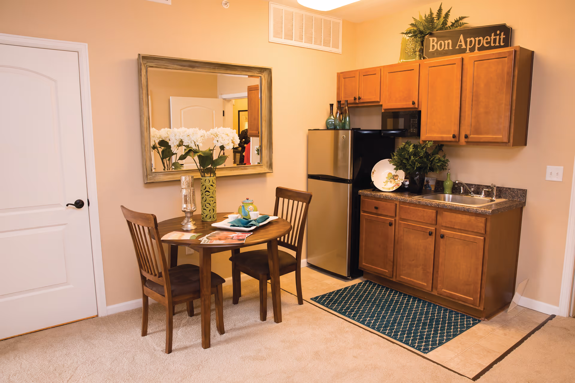 Small kitchenette and dining area with wooden cabinets, a refrigerator, sink, and a round table with two chairs.