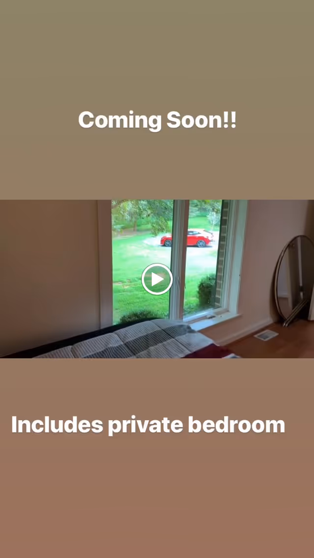 View of a bedroom corner with a bed partially visible, a large window showing green grass and a red car outside, and a round mirror resting on the floor against the wall.