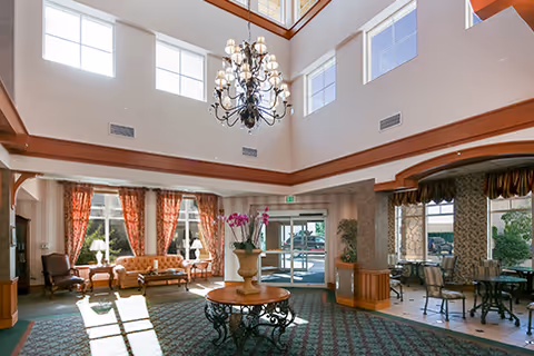 Two-story reception lobby with a central chandelier, round table, seating area, and glass entry doors.
