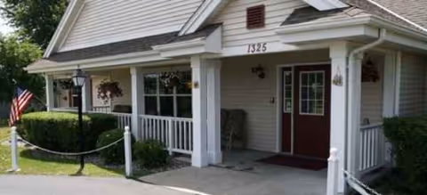 Front view of Summit Ridge Place building with porch, railing, flag, and shrubs.