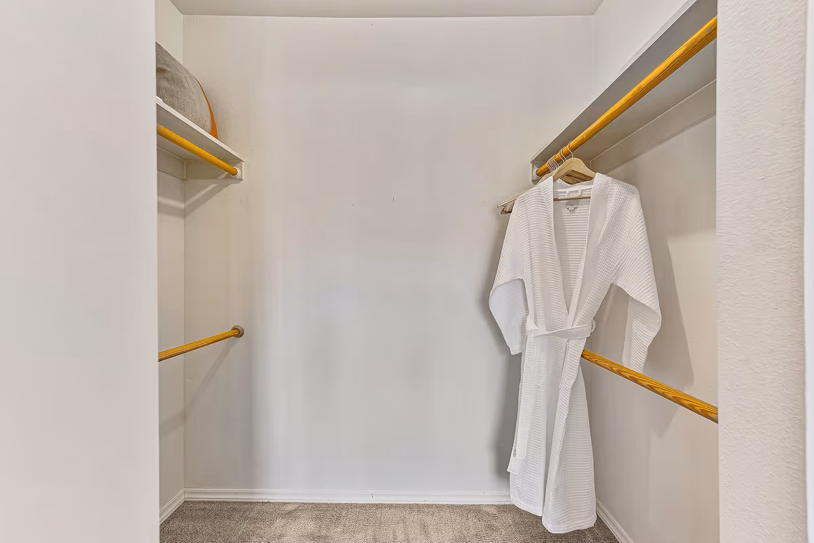 Walk-in closet with wooden hanging rods and a white robe hanging on the right.