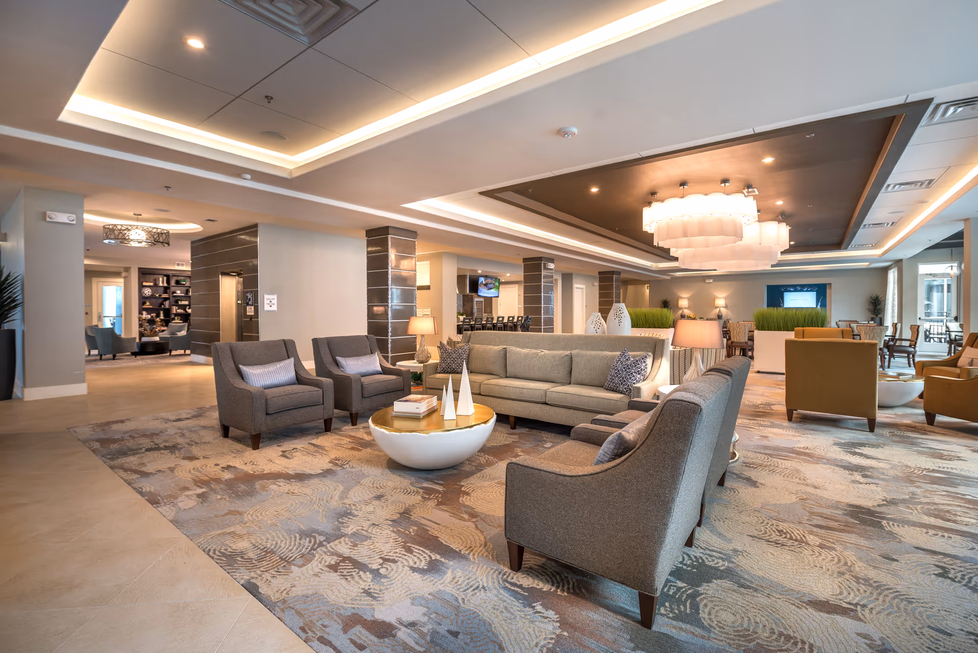 Spacious modern communal lounge with sofas, armchairs, coffee tables, and decorative lighting.
