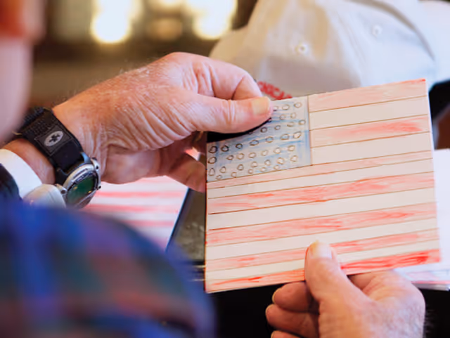 Close-up of an elderly person's hands holding a handmade American flag drawing colored with red and blue crayons or markers.