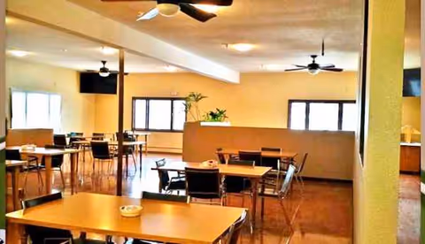 Spacious dining room with tables, chairs, and ceiling fans in a senior facility.