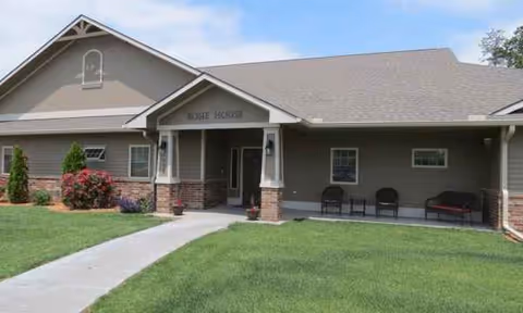 Senior living facility building front with covered entrance, lawn, and seating.
