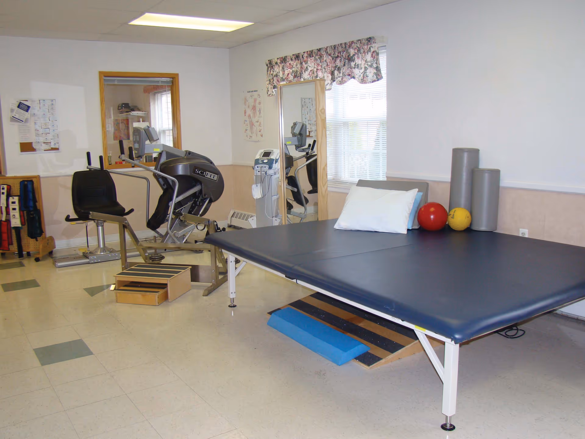 Physical therapy/exercise room with a large treatment table, exercise equipment, therapy balls, and foam rollers.