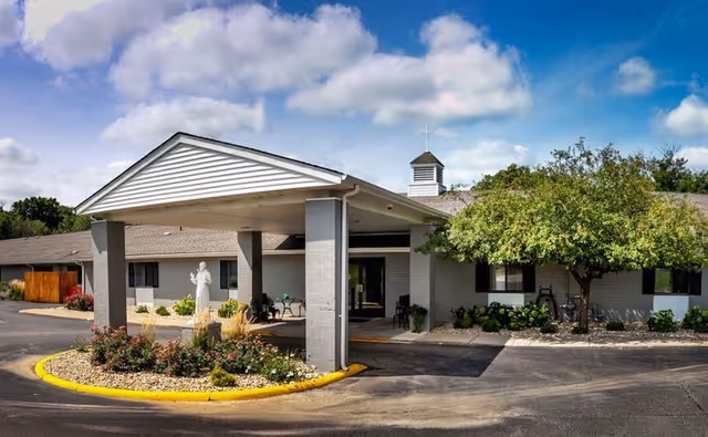 Front entrance of the St. Francis Woods building with a covered drop-off, landscaped island and a statue.