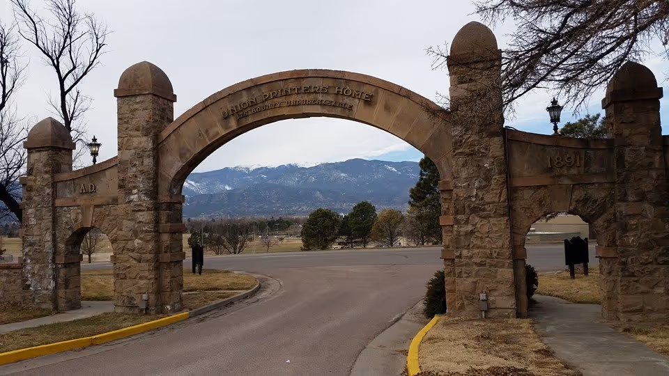 Stone arched entrance gate reading 'Union Printers Home' spanning a road with mountains visible in the background.