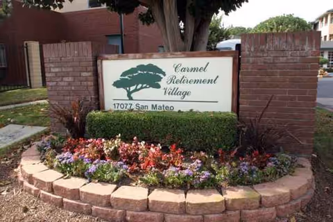 Carmel Retirement Village sign framed by brick posts and a colorful flower bed.