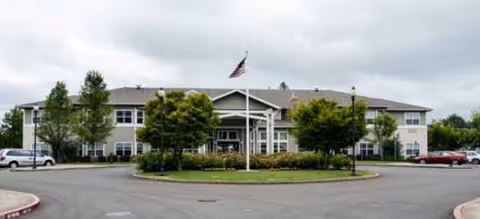 Meadowlark Senior Living building with circular driveway, flagpole, trees, and parked cars.