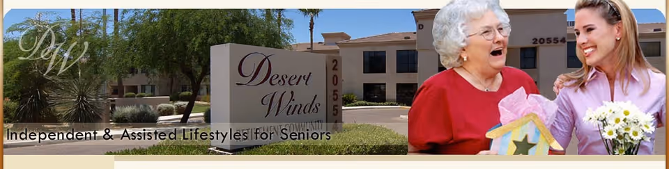 An outdoor view of the Desert Winds Independent Living facility sign with a building and palm trees in the background. To the right, an elderly woman in a red top is smiling and holding a decorative birdhouse, while a younger woman in a pink shirt stands beside her holding a bouquet of white flowers.