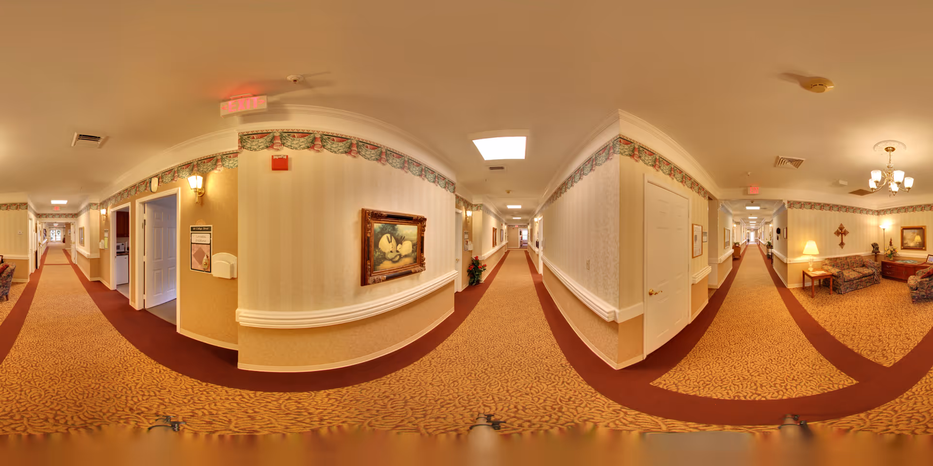 Carpeted senior living facility hallway with patterned wallpaper, framed artwork, seating area, and multiple doorways.