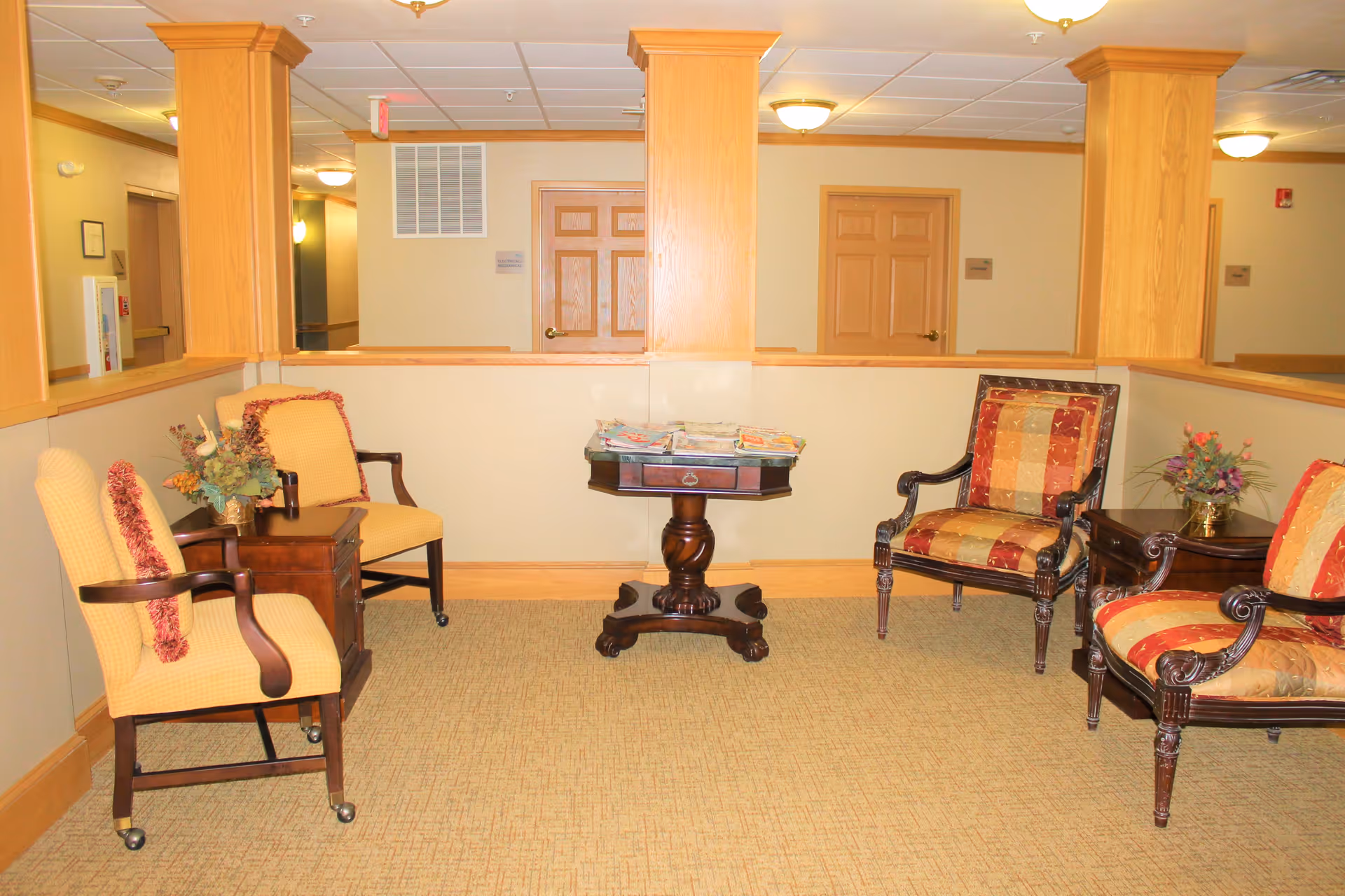Small common seating area with upholstered chairs, a central table with magazines, and floral arrangements.