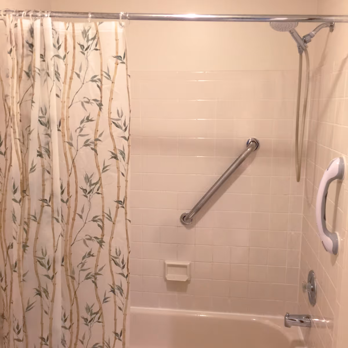 Bathtub shower with white tile, a floral shower curtain, grab bars, and a handheld showerhead.
