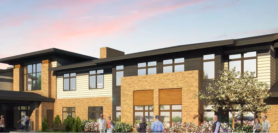 Front exterior of a modern two-story brick and siding senior living building with people and landscaped gardens under a colorful sky.