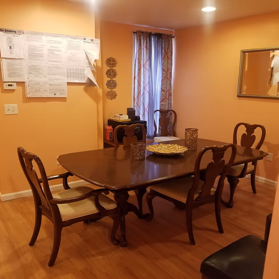 Dining room with a dark wooden table and six chairs, peach-colored walls, a curtained window, and papers posted on the wall.