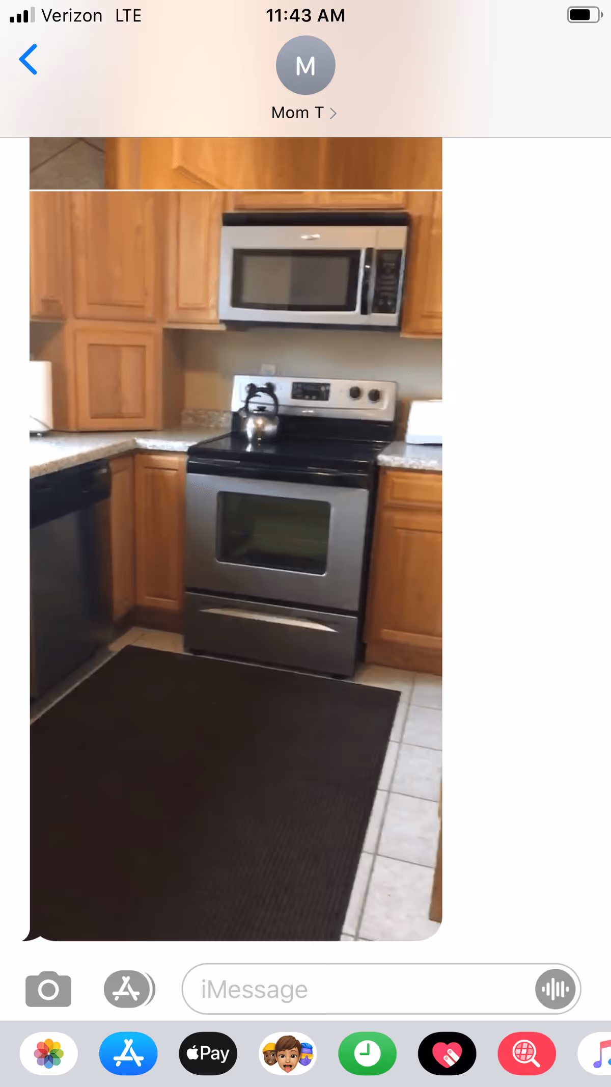 A kitchen with wooden cabinets, a stainless steel oven with a kettle on top, a microwave above the oven, a dishwasher to the left, and a dark floor mat on the tiled floor.